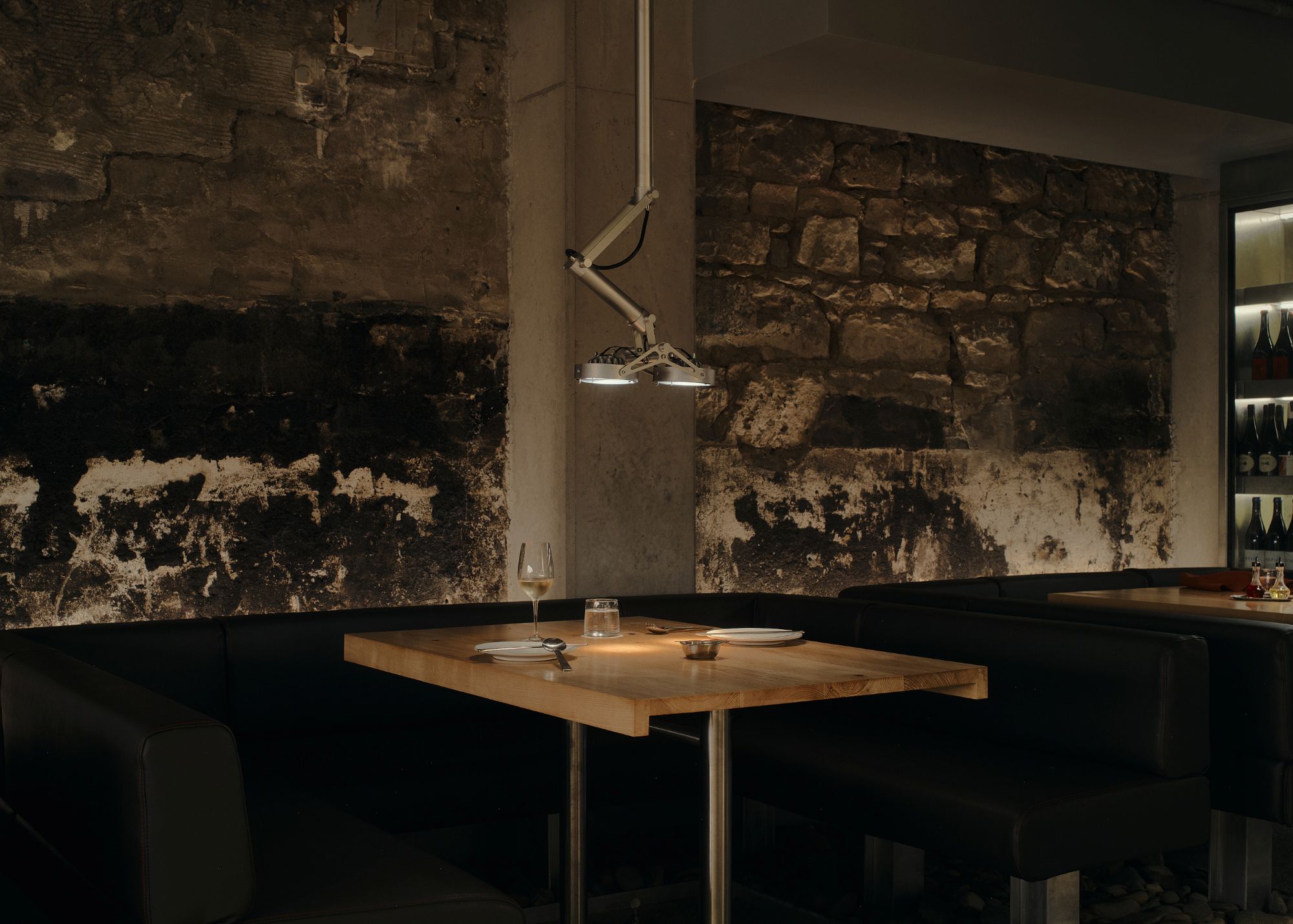 a table at a restaurant with a wooden surface holding two plates and a wine glass, all underneath an industrial ceiling light