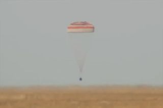 Russian Soyuz capsule under parachutes during cosmonaut landing as ground approaches