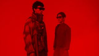 Two people looking at each other, they're drenched in red light and wearing the Xreal Air AR Glasses