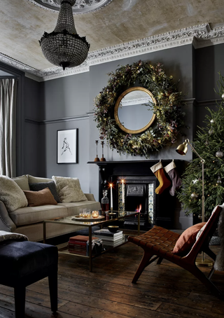 A Christmas-themed living room with black wall decor, statement black ceiling chandelier light, cream upholstered sofa, and mirror framed with foliage