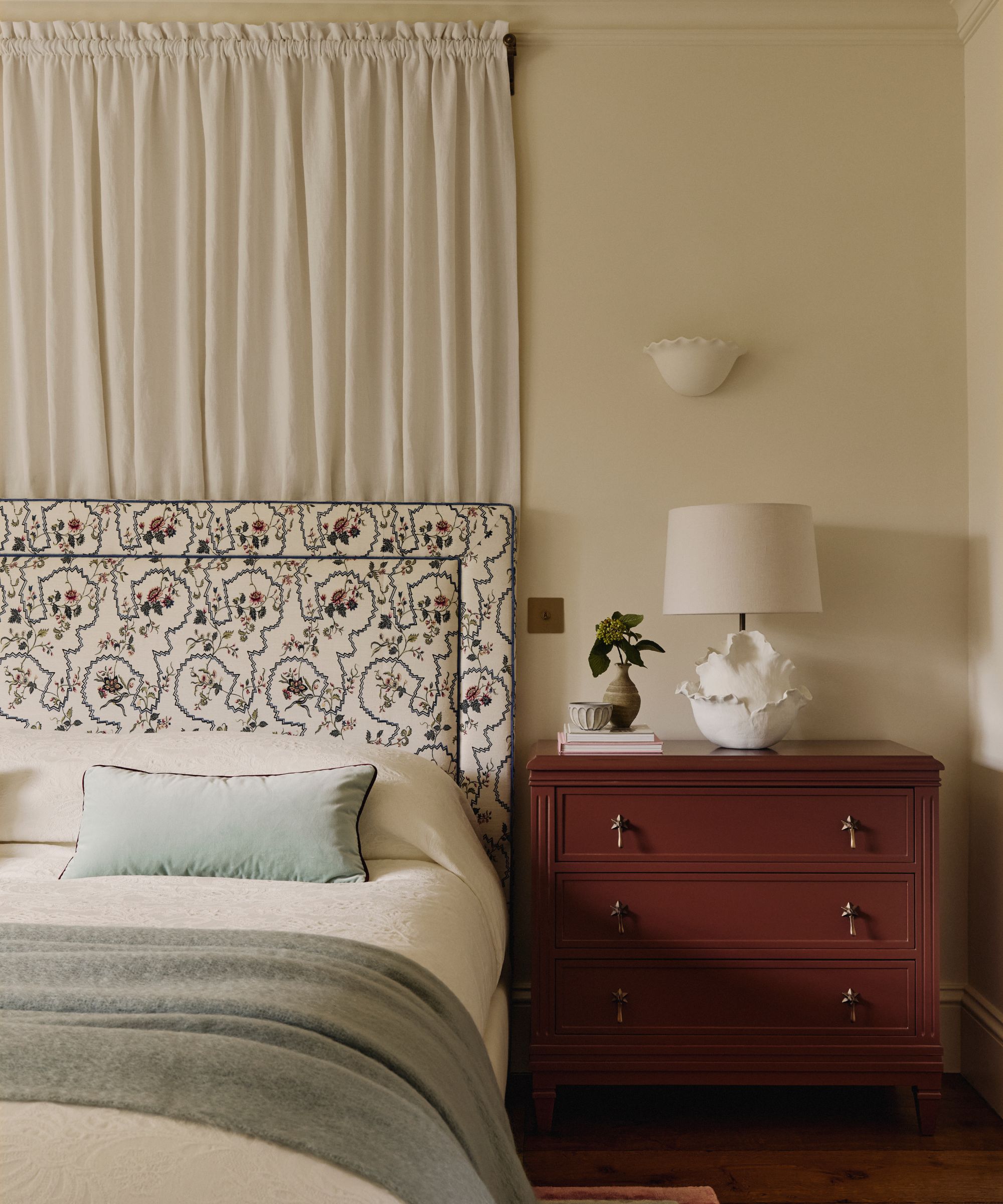 neutral bedroom with a bed canopy and floral headboard with a large chocolate brown painted nightstand drawers
