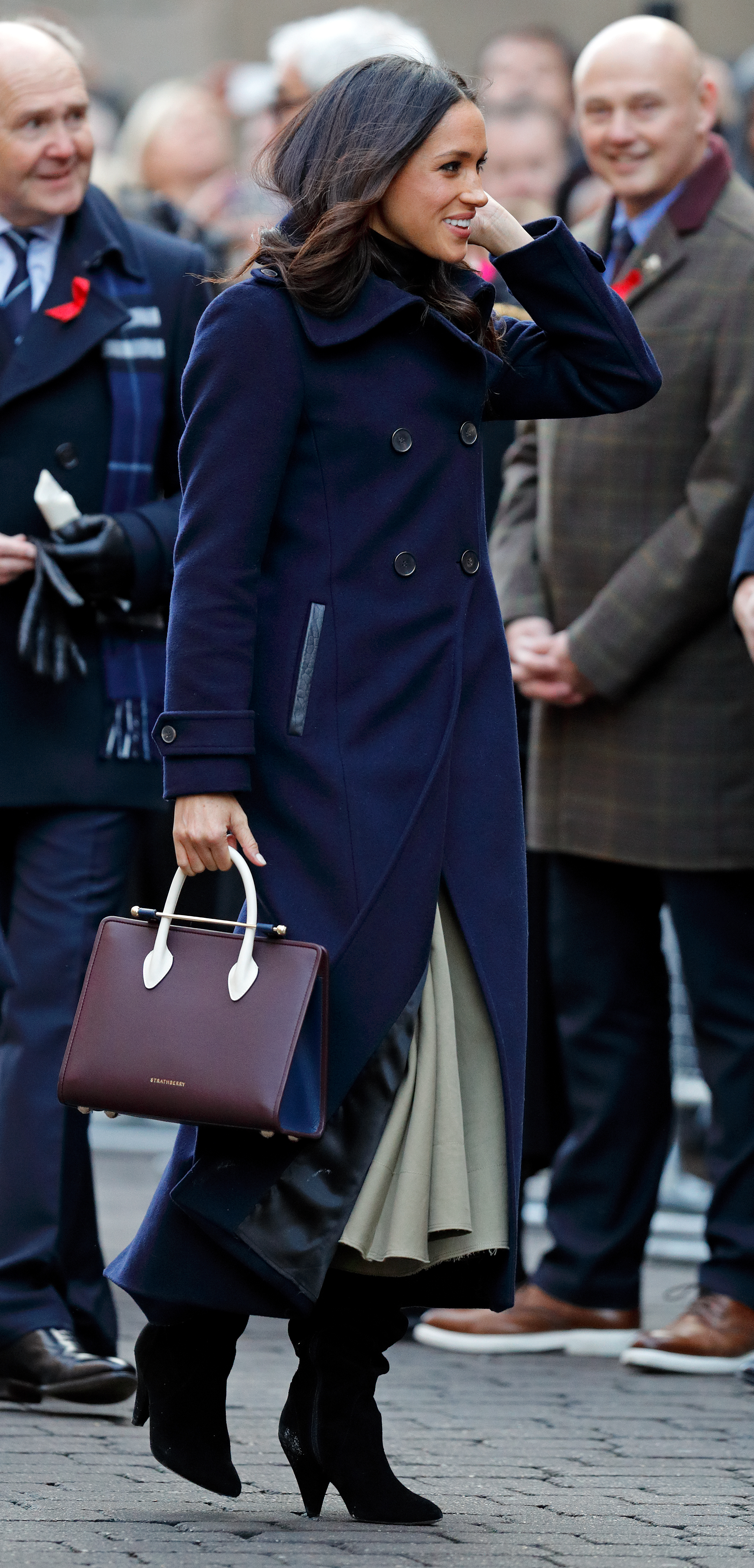 Meghan Marle wearing a blue coat carrying a burgundy Strathberry bag