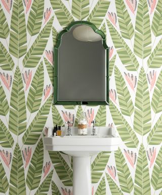 Bathroom sink with green and pink palm print wallpaper behind it