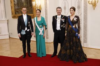 Queen Mary wearing a black and gold ballgown standing next to King Frederik and the President of Finland Alexander Stubb (L) and his spouse Suzanne Innes-Stubb at a state banquet in March 2025