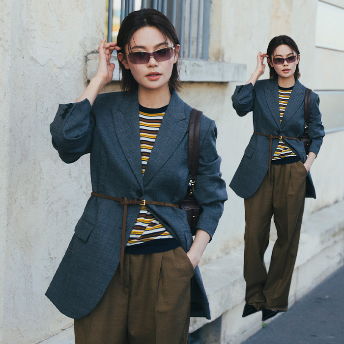 Woman wears striped shirt, gray blazer, olive green trousers, and pointed toe shoes. 