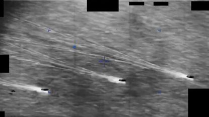 Three ships on a gray sea spot a hovering object in this DoD video