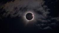 the moon perfectly obscures the sun, leaving a ring of white fiery light in a slightly cloudy sky