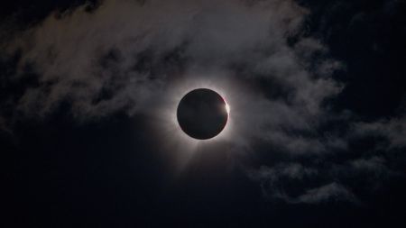 the moon perfectly obscures the sun, leaving a ring of white fiery light in a slightly cloudy sky