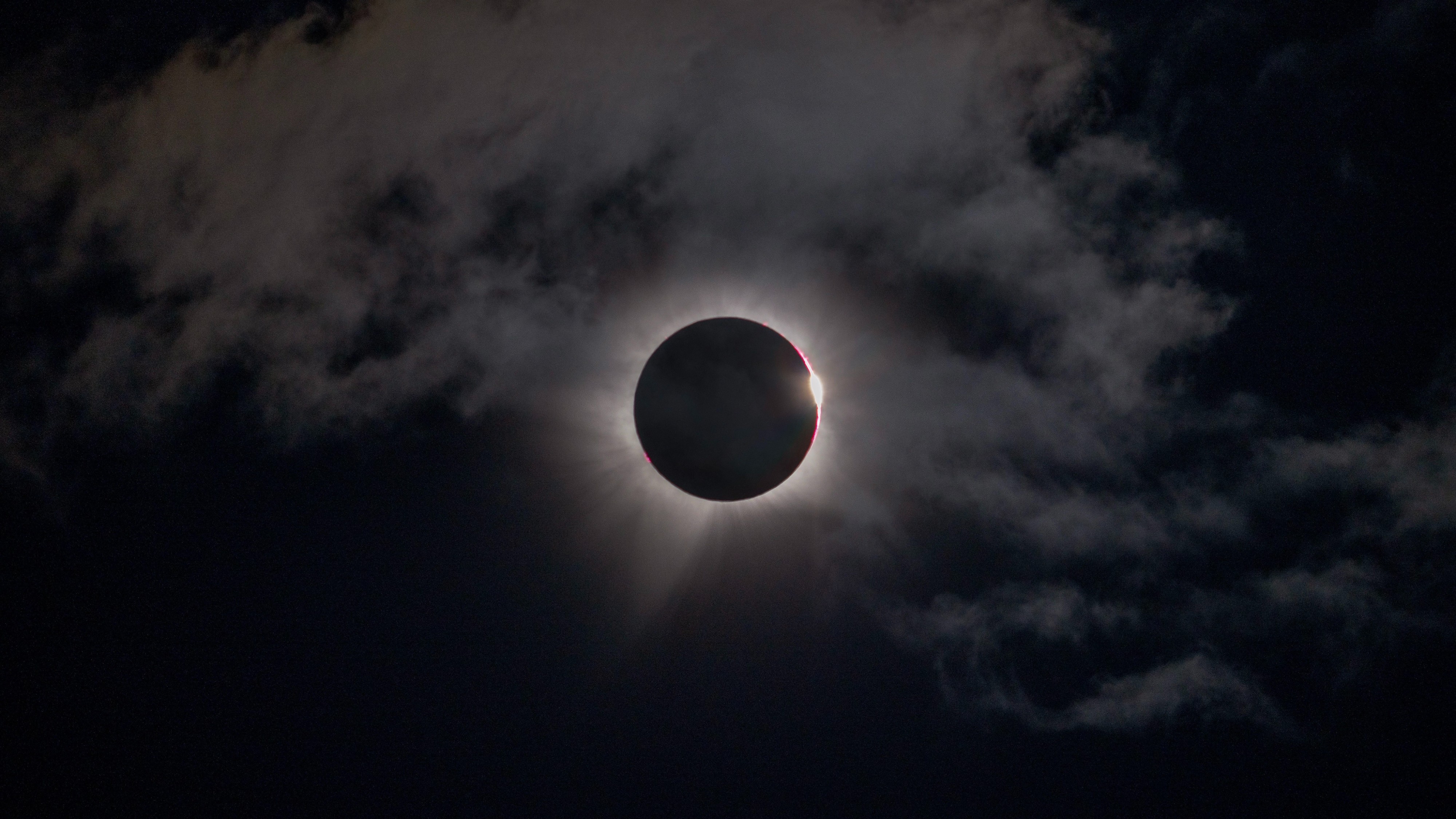 the moon perfectly obscures the sun, leaving a ring of white fiery light in a slightly cloudy sky