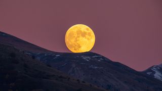 a large full moon rises over a mountain range