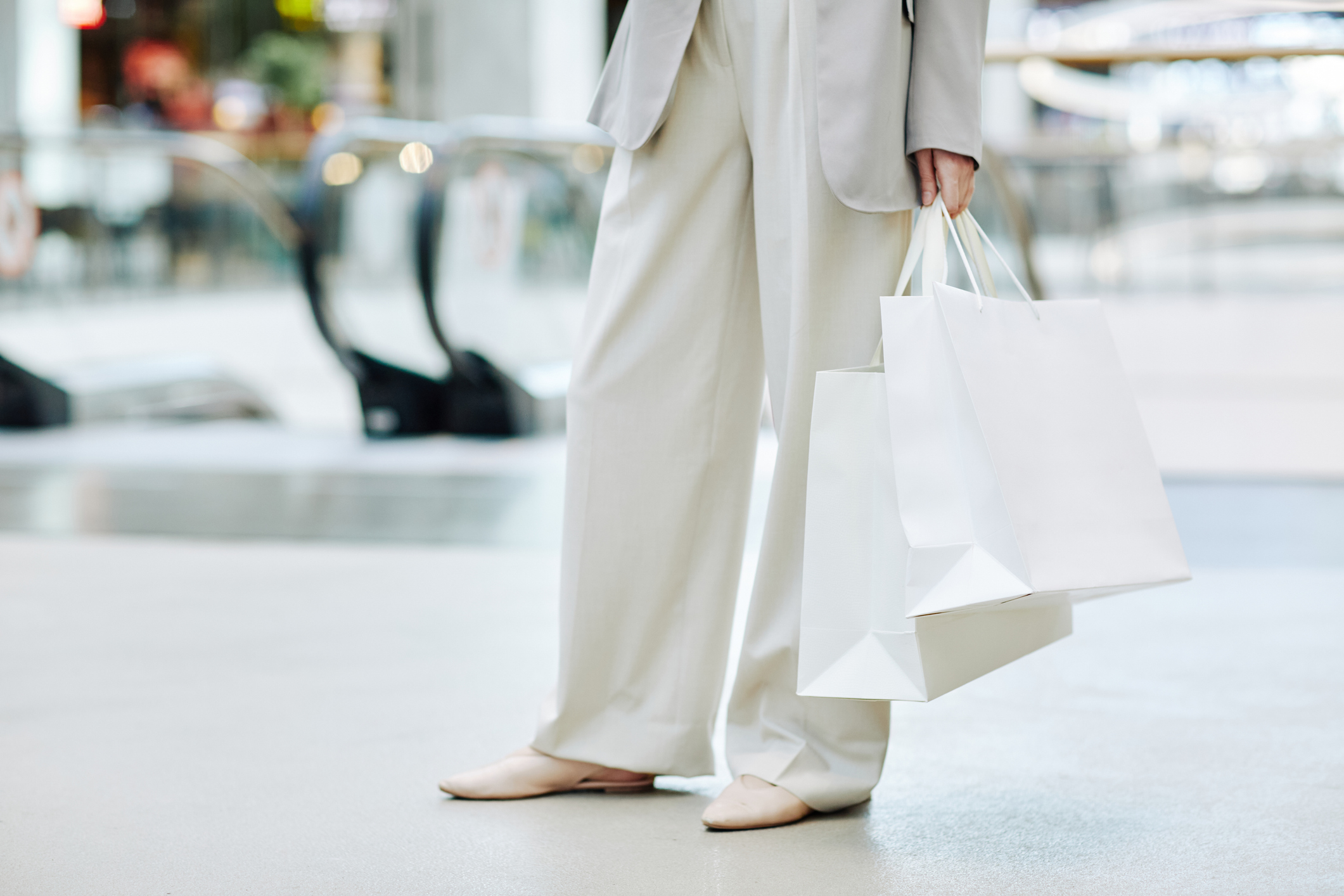 Minimal lower section of elegant woman wearing pants suit and holding blank shopping bags in mall