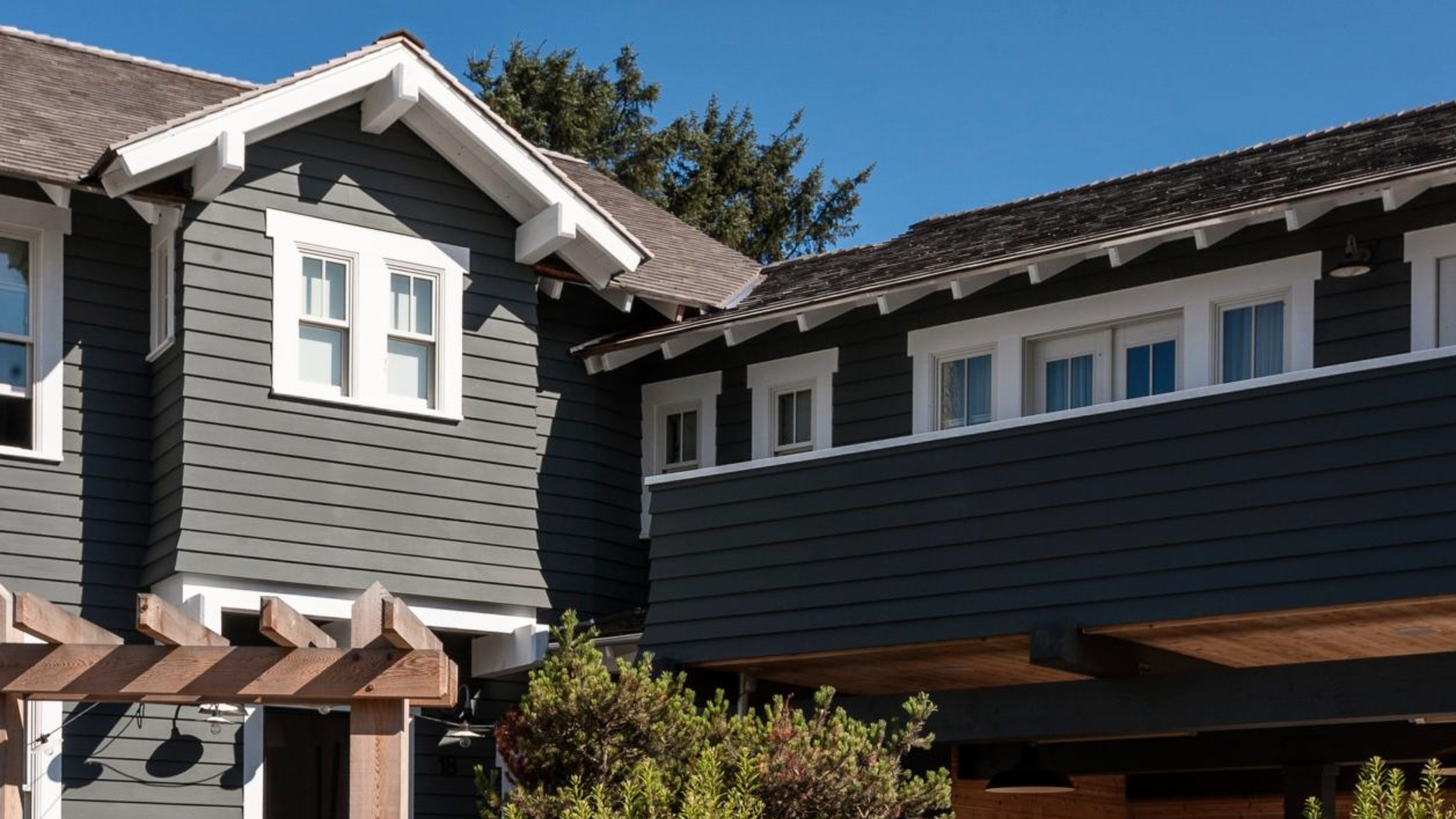 Close-up image of the top of the exterior of a house that is painted in a dark gray with white trim. There are lots of windows.