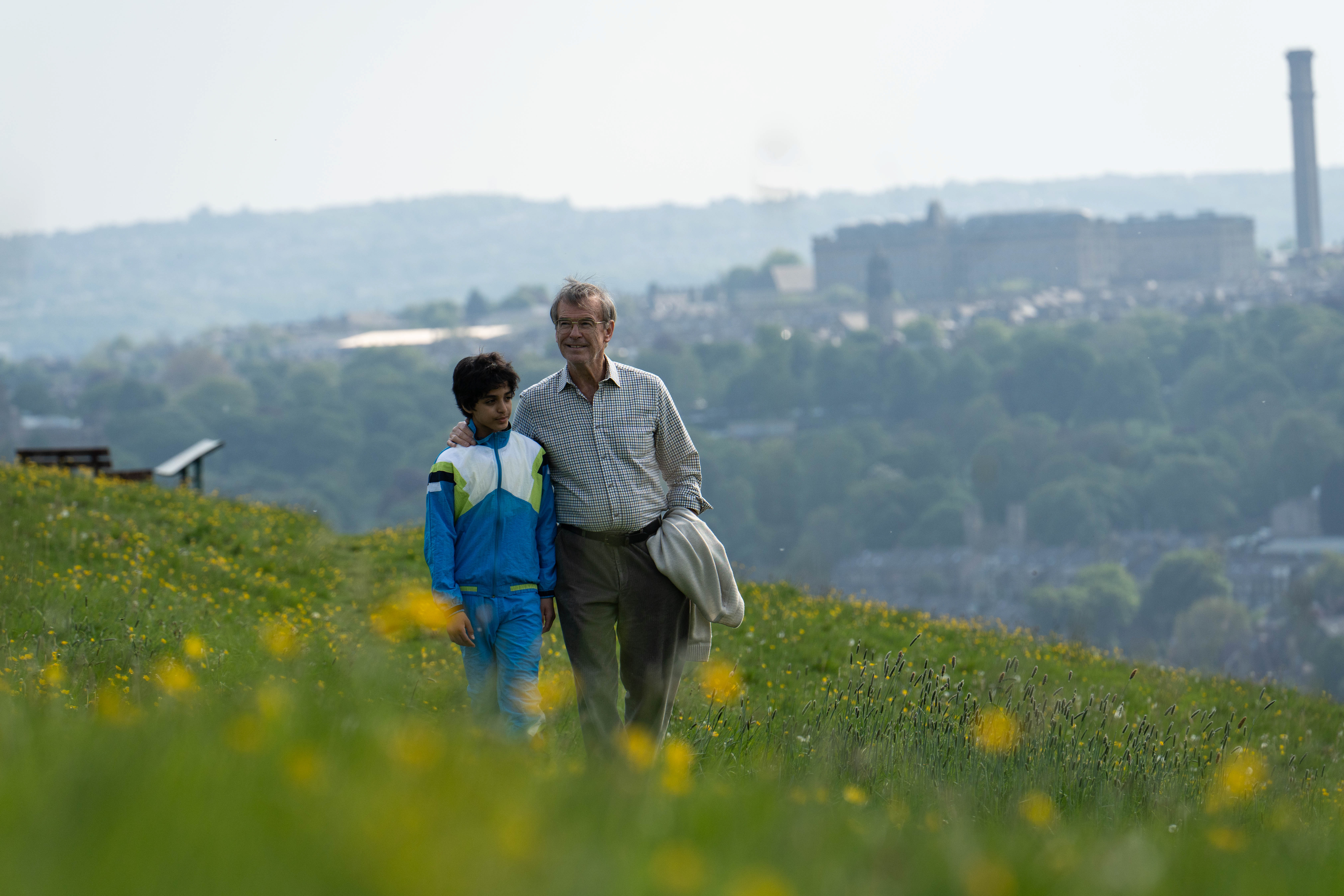 a production image of pierce brosnan as brenden ingle walking with a young, seven year old naz hamed across the hills of sheffield