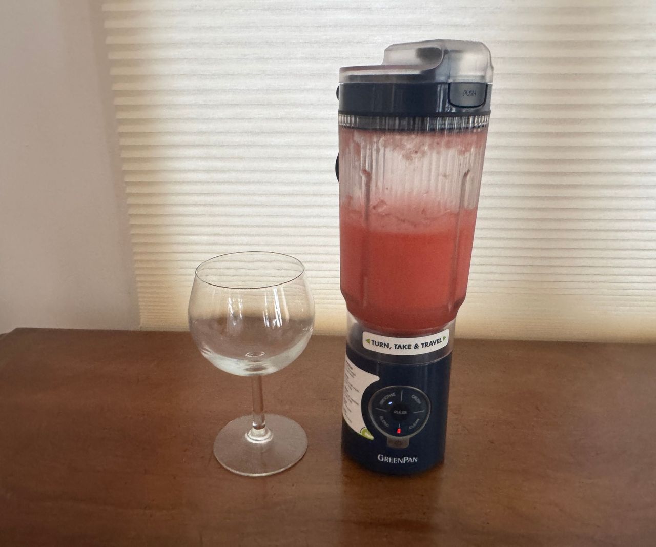 A pink liquid in a black portable blender beside a drinking glass.