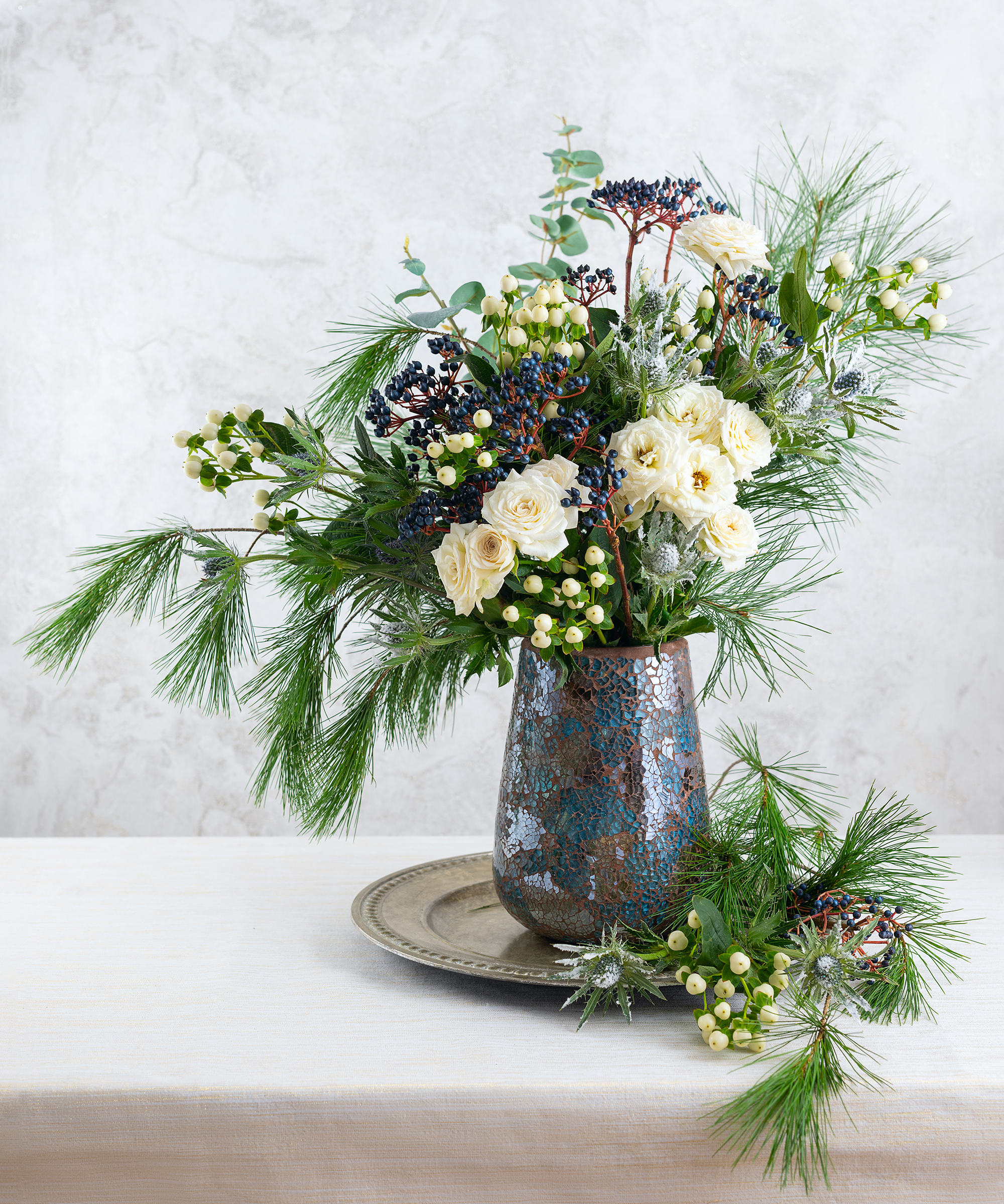 Beautiful winter bouquet in vase. Flower arrangement with roses, fir branches, winter berries, eucalyptus and eryngium.