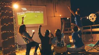 friends cheering around outdoor projector as they watch the football