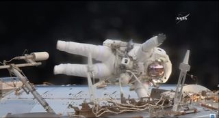 Figure in spacesuit waves while hanging outside the space station.