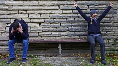 At one end of a bench, a young man looks disappointed and glum. On the other end, a young woman celebrates.