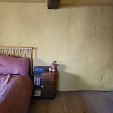 yellow bedroom with bed, wooden bedside table and rope skirting