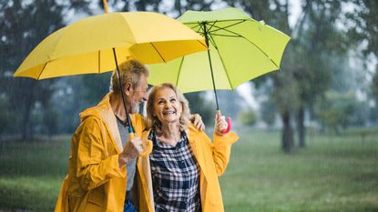 Happy mature couple in yellow raincoats walking under umbrellas on a rainy day