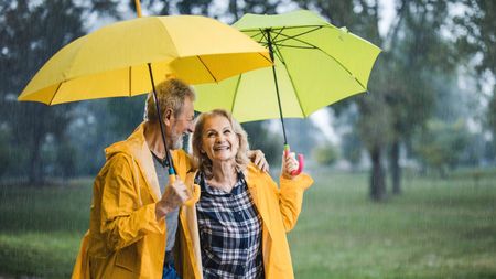 Happy mature couple in yellow raincoats walking under umbrellas on a rainy day