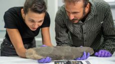 We see a woman and a man looking at a long hand ax in the lab.