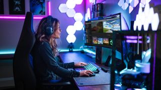 Kvindelig Xbox Game Pass-medlem med hovedtelefoner sidder ved et skrivebord med tastatur, mus og en skærm og kigger på sit PC Game Pass-bibliotek
