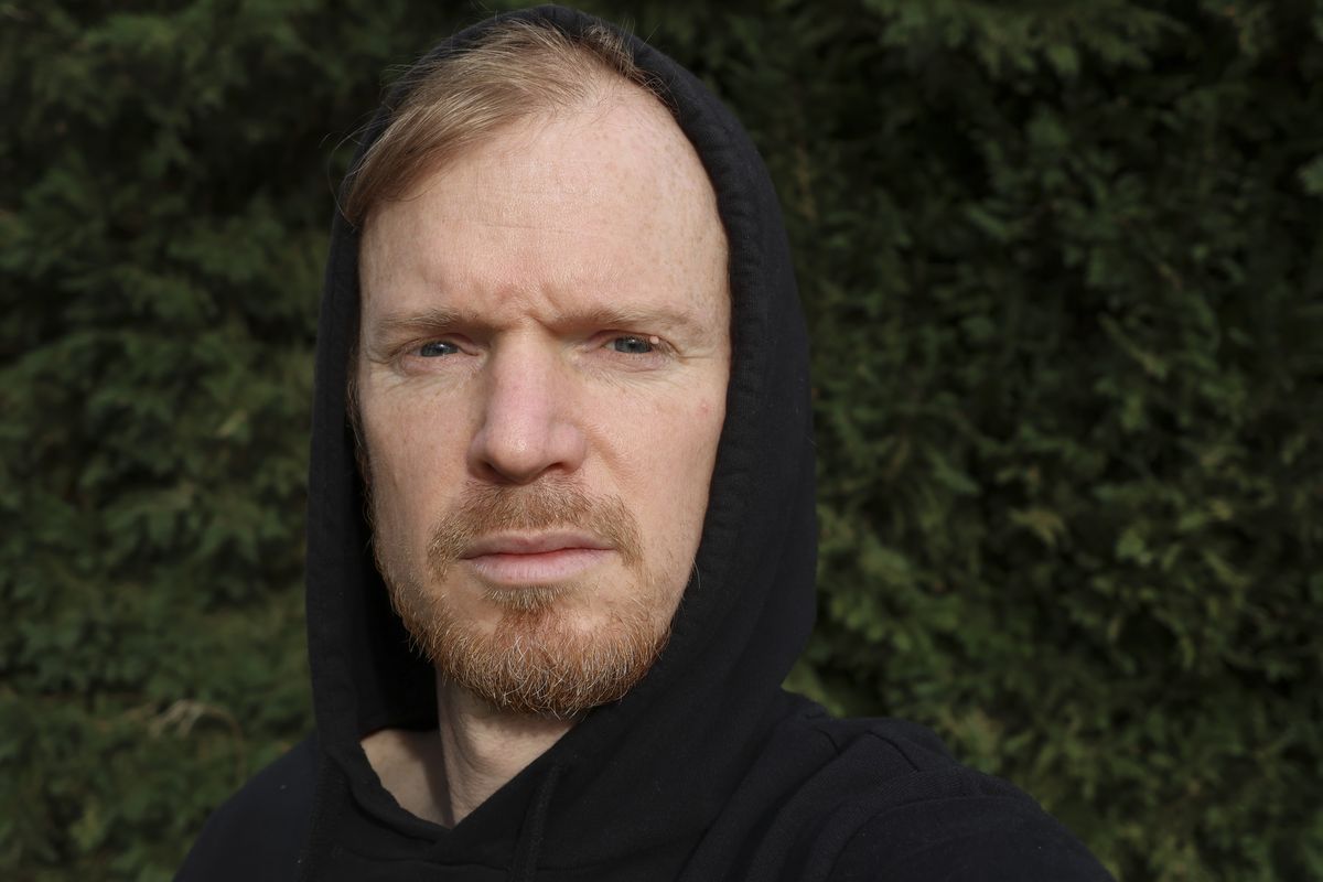 A selfie of a man in a black hoodie with foliage background