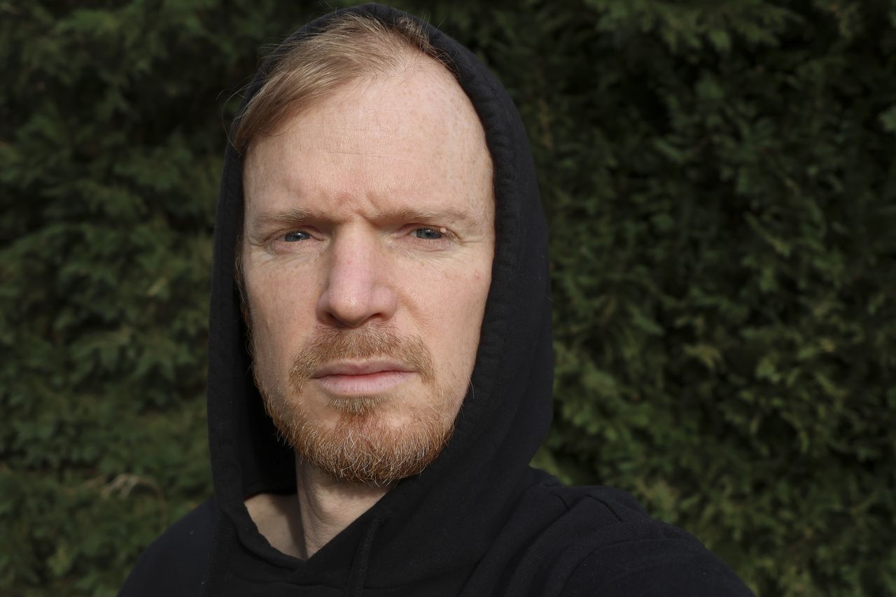 A selfie of a man in a black hoodie with foliage background