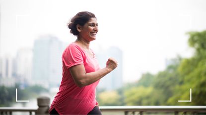 Woman running and smiling along a river path to represent low intensity training as part of 80/20 running