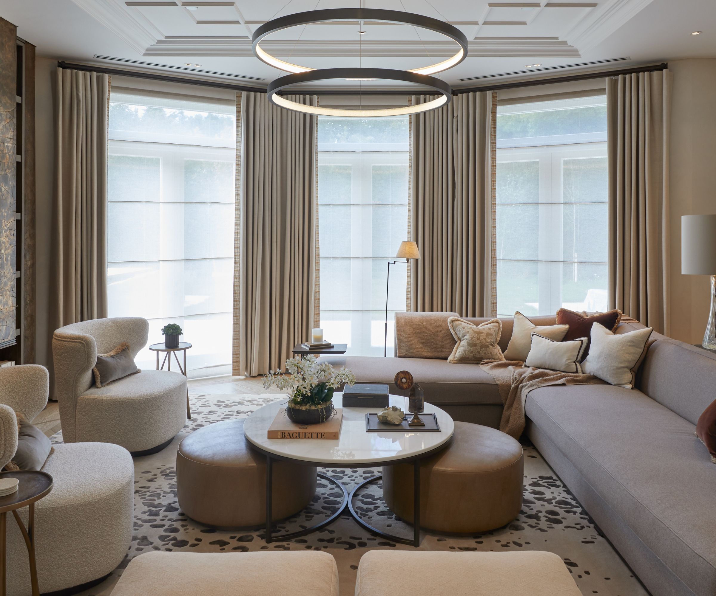 Modern living room with round, sculptural chanelier, large floor to ceiling windows with cream curtains, neutral seating, coffee table and rug
