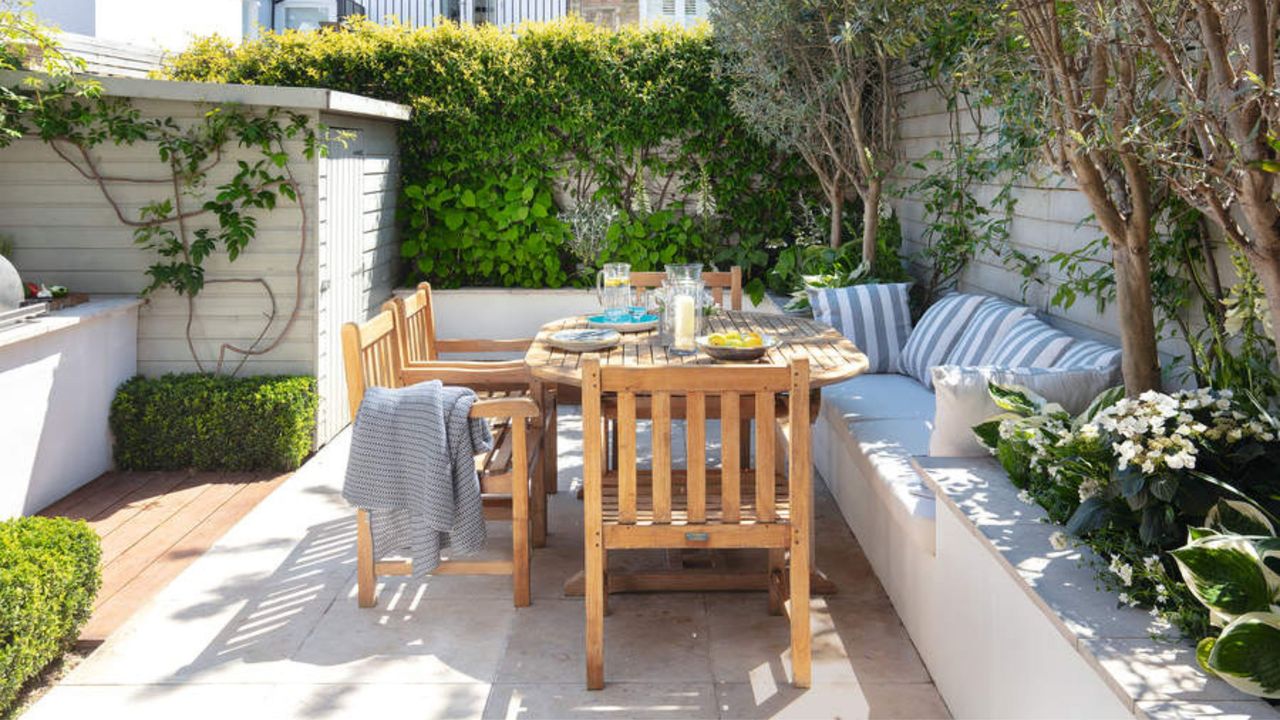 Garden in Fulham, paved with raised beds, wooden table, chairs and inbuilt seat with striped cushions. Susan and Henry Parker&#039;s garden at their four bedroom Victorian house in Fulham, London.