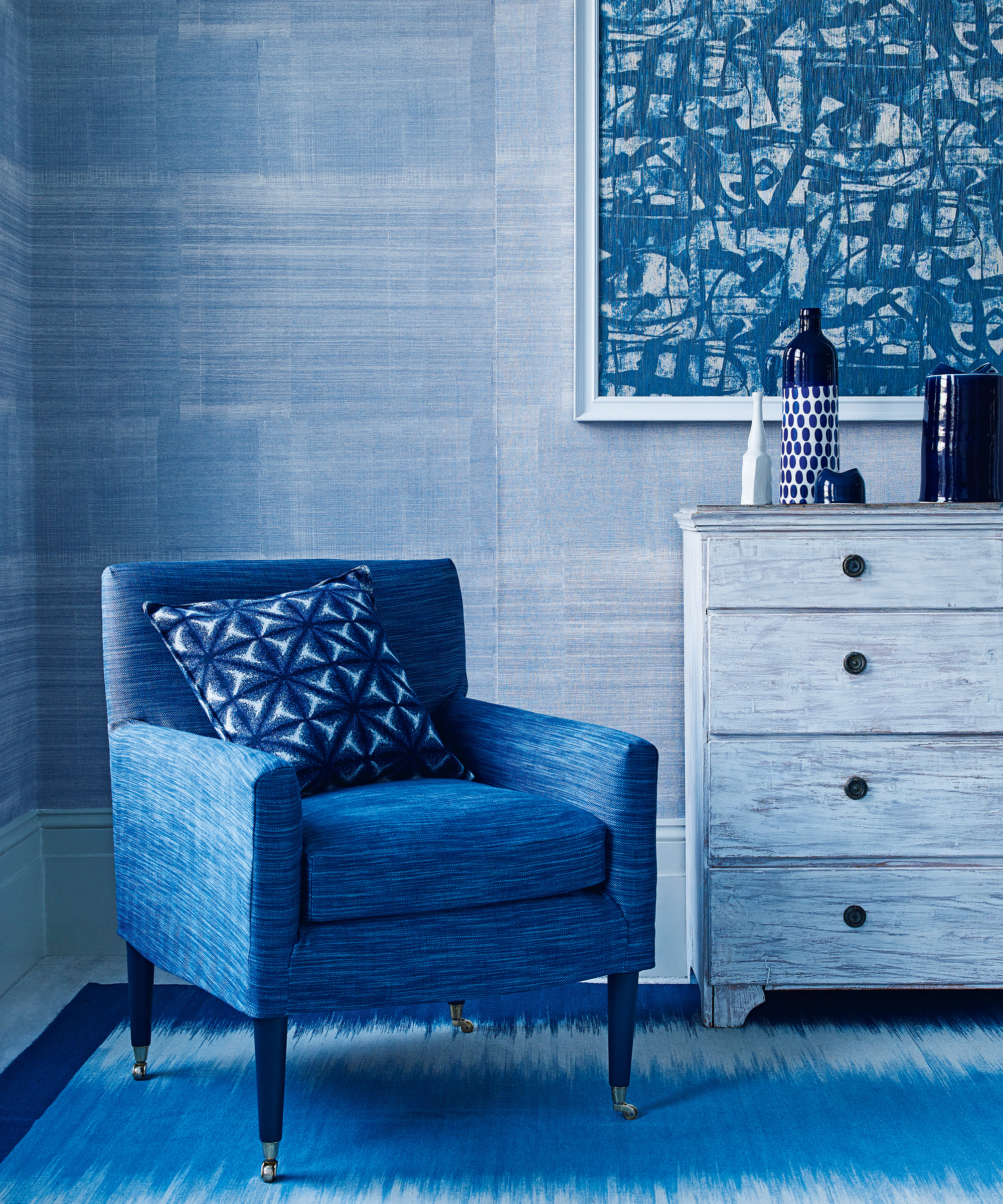 A blue living room with blue armchair, walls, rug and drawers.