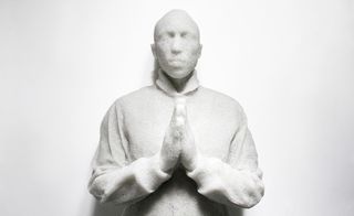 A close-up of a life-sized cast of Pharrell Williams with his hand put together in a praying motion.