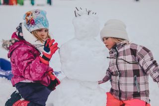 How to help your kid sleep on Christmas Eve, featuring two girls building a snowman outside