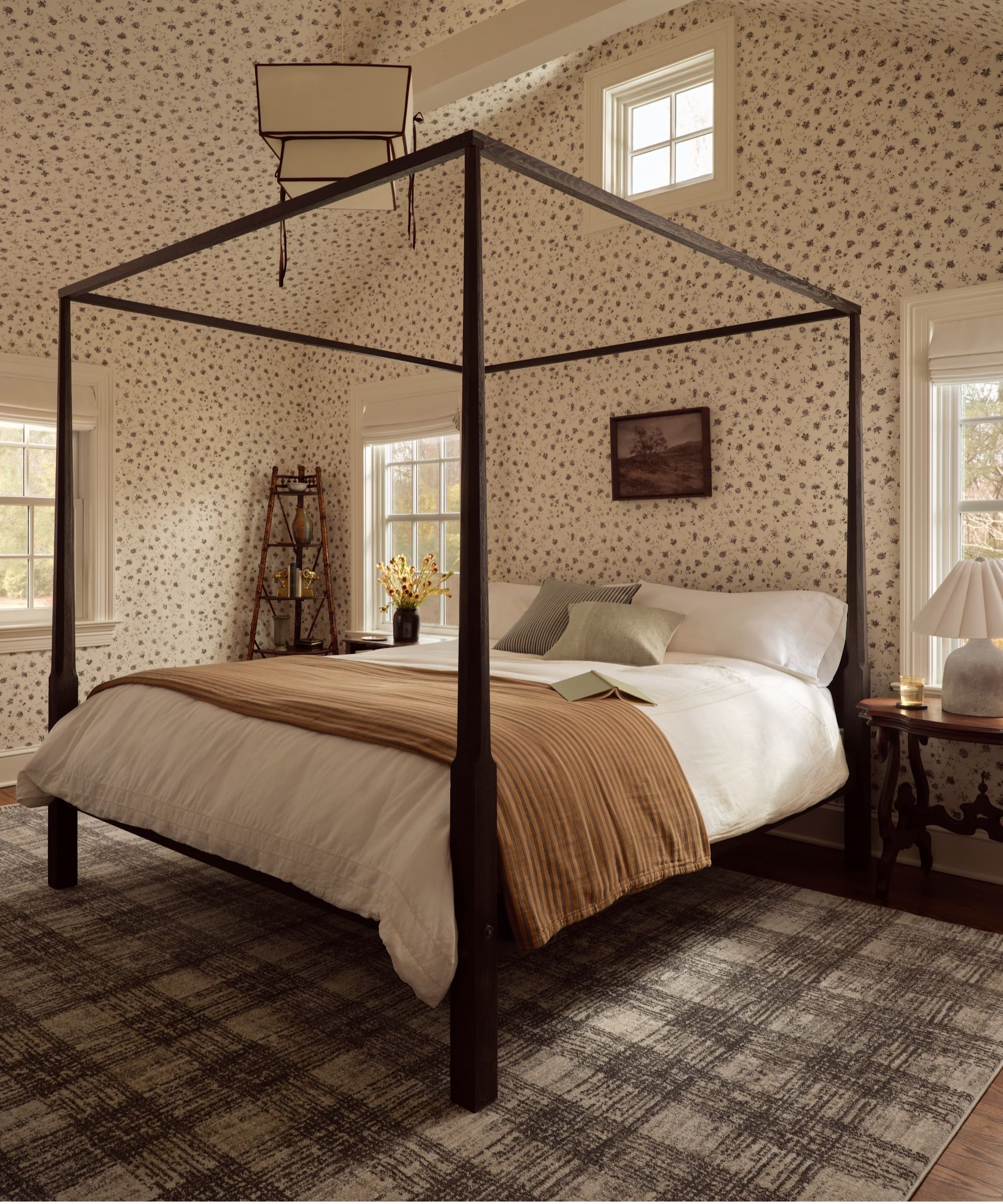 bedroom with black four posted bed, ditsy floral walls and ceiling with a neutral and beige styled bed and a plaid grey brown rug underneath