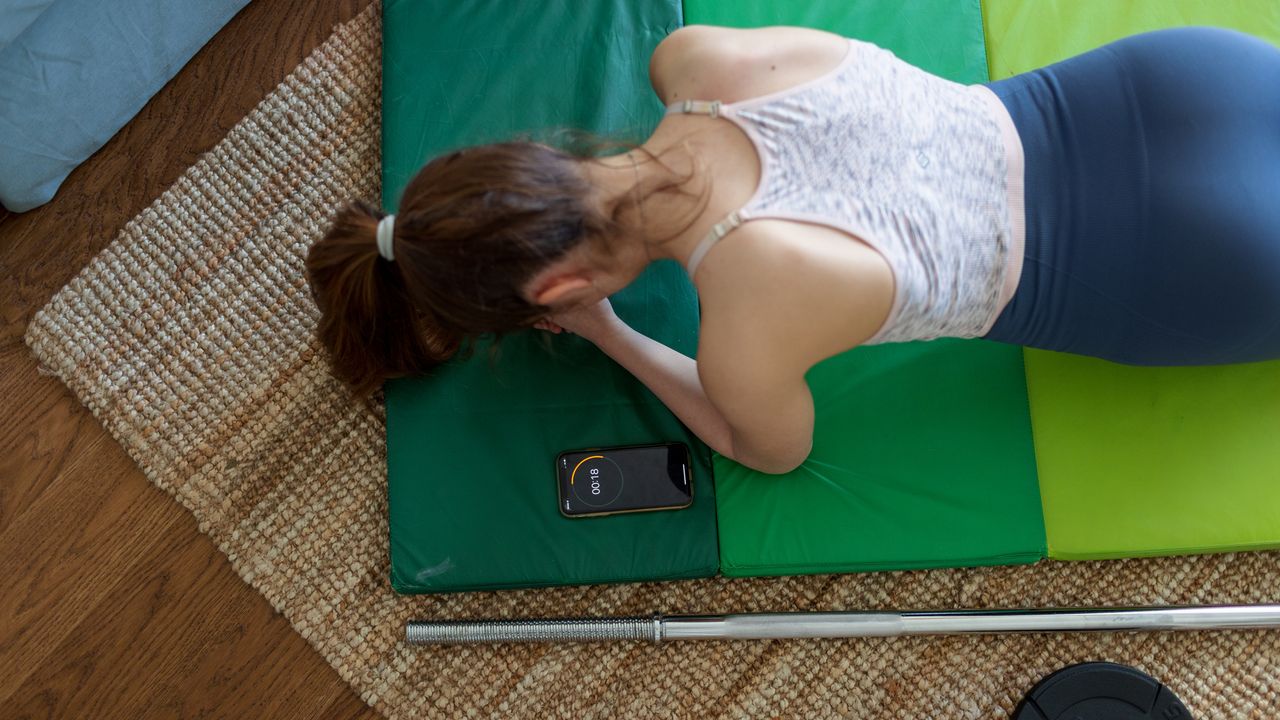 Woman seen from above holding a plank, a smartphone is next to displaying 18 seconds left on a timer