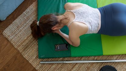 Woman seen from above holding a plank, a smartphone is next to displaying 18 seconds left on a timer