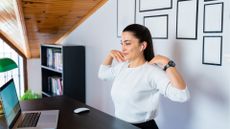 white woman white long sleeved top fingertips on shoulders in front of laptop office background