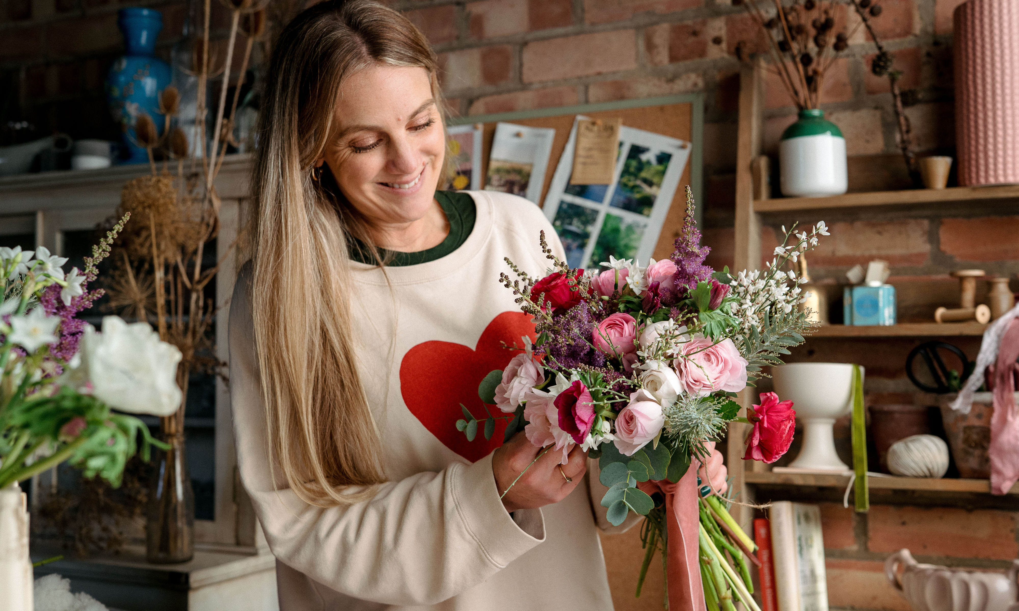 Woman holding a handtied bouquet wearing cream jumper with a large red heart on it