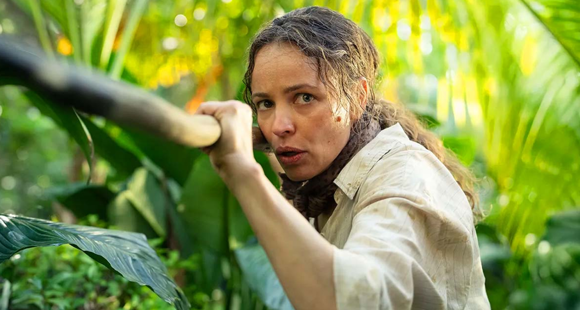 rachel mcadamas walks through a palm tree covered jungle holding a spear in a still from the 2026 survival thriller send help