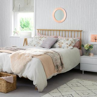 A modern cosy bedroom, with grey patterned wallpaper, double bed and small mirror, rug and window with patterned grey blinds.