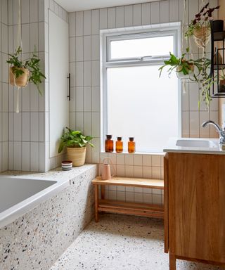 pared back bathroom with terrazzo floor tiles and white metro tiles on wall with hanging house plants