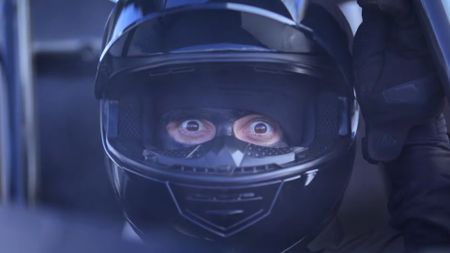 A racecar driver lifts his visor and stares, bug-eyed, at the viewer in an ad for Sonic Racing: CrossWorlds