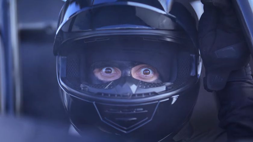 A racecar driver lifts his visor and stares, bug-eyed, at the viewer in an ad for Sonic Racing: CrossWorlds