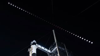 a time lapse of a total lunar eclipse is captured above a launch pad and a rocket waiting to lift off.