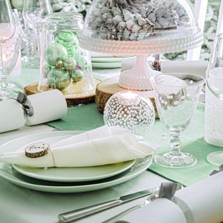 A dining table set for a Christmas dinner with a white colpour scheme and a napkin folded into a point