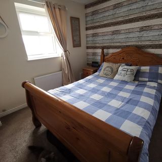 Bedroom with wood panel style wallpaper and wooden bed with blue checkered duvet