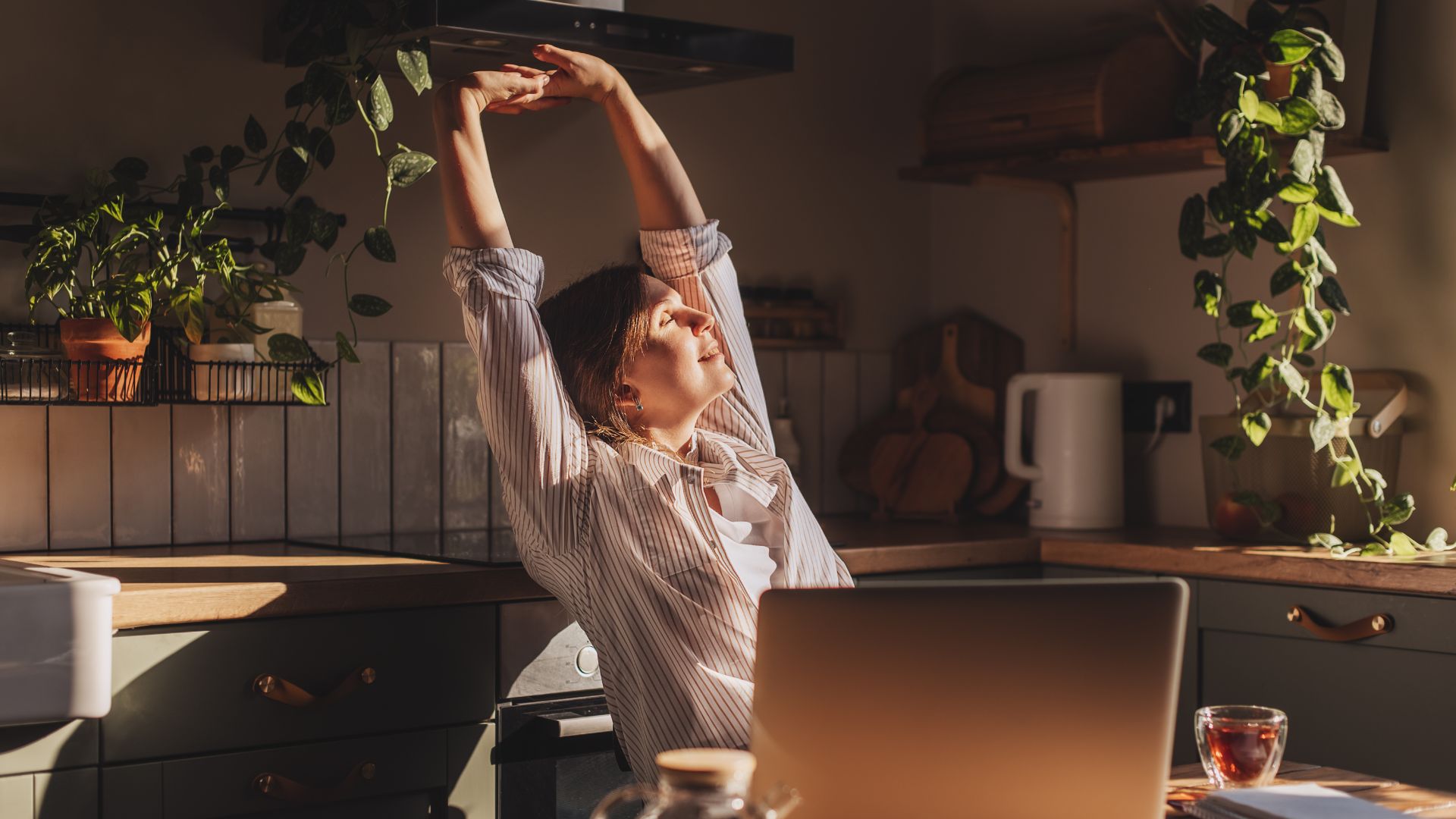 Woman stretching arms up to the sky, happy face, in the morning drinking coffee