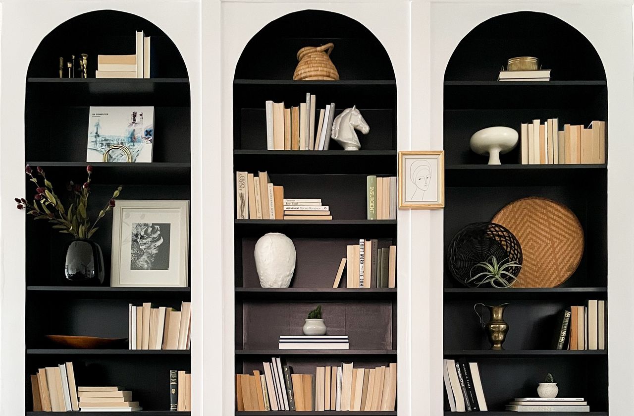 White arched shelving decorated with books with the inside of the shelves painted black